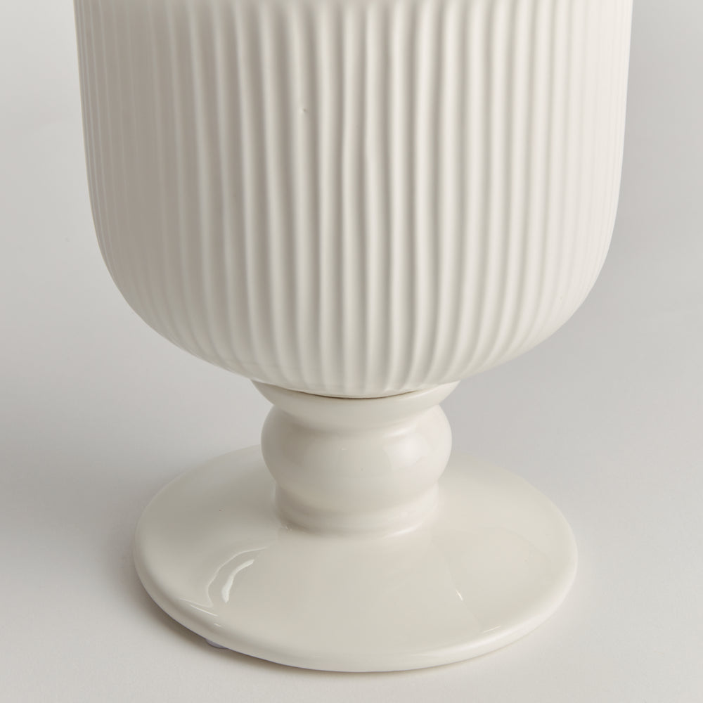Detail of the small white ceramic footed cachepot showing ribbed sides and a rounded pedestal foot on white, Traditional