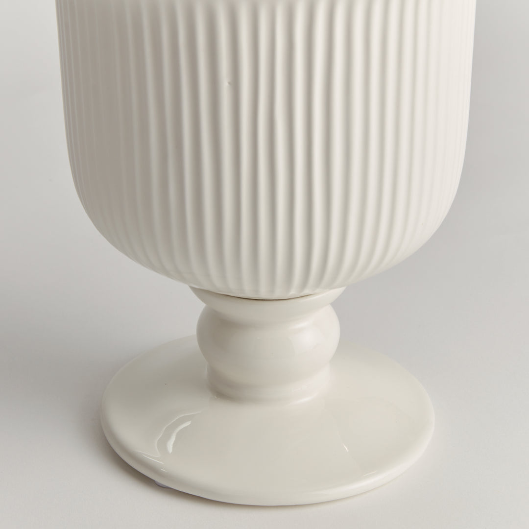 Detail of the small white ceramic footed cachepot showing ribbed sides and a rounded pedestal foot on white, Traditional
