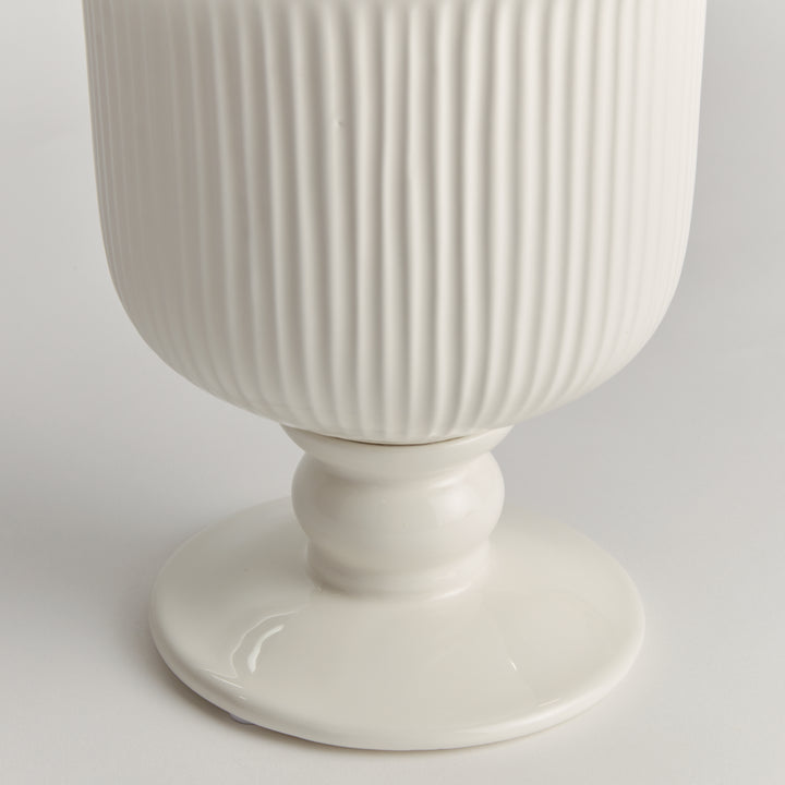 Detail of the small white ceramic footed cachepot showing ribbed sides and a rounded pedestal foot on white, Traditional