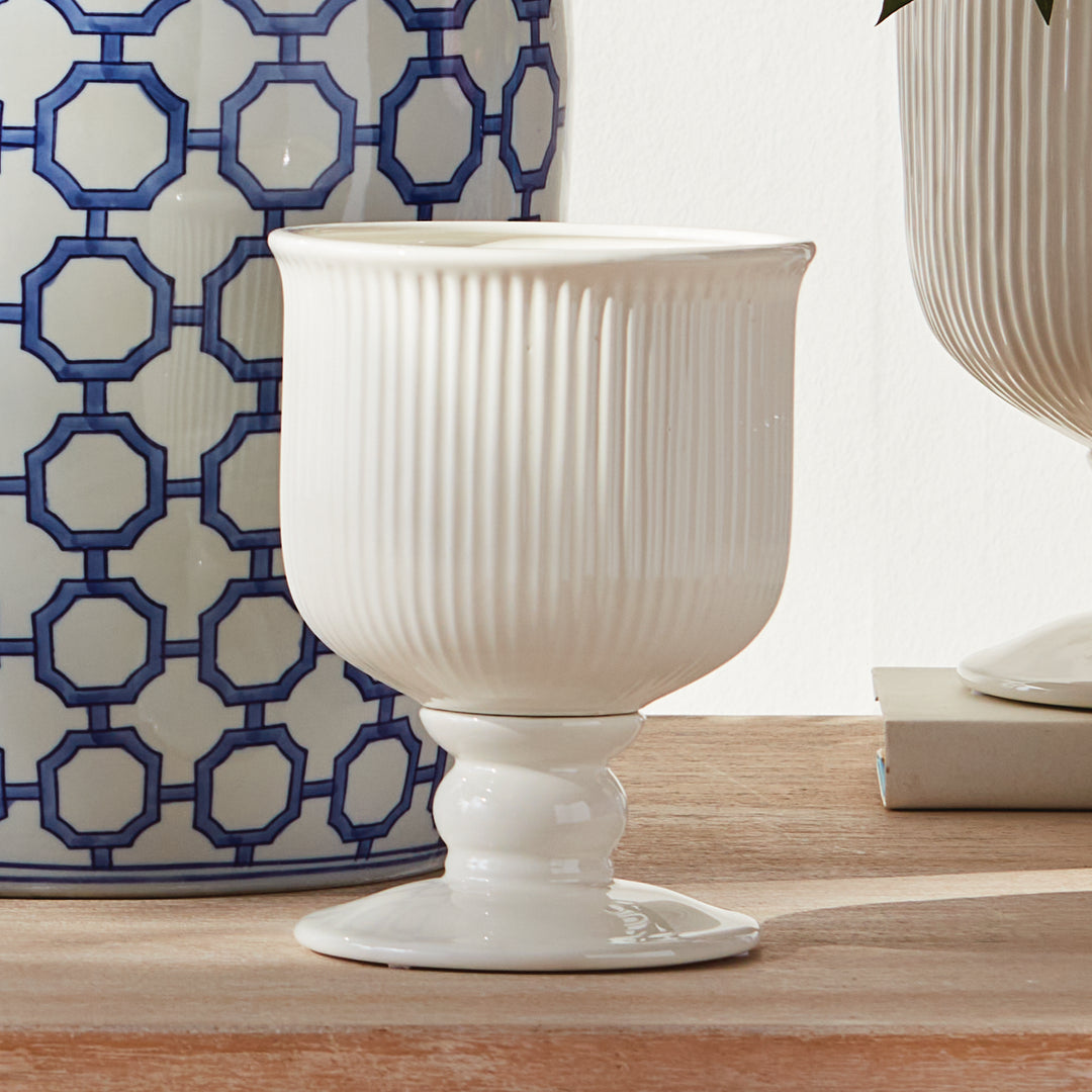 Small white ribbed ceramic footed cachepot displayed on a wood surface beside blue patterned decor and pottery, Traditional