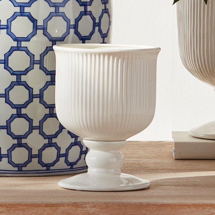Small white ribbed ceramic footed cachepot displayed on a wood surface beside blue patterned decor and pottery, Traditional
