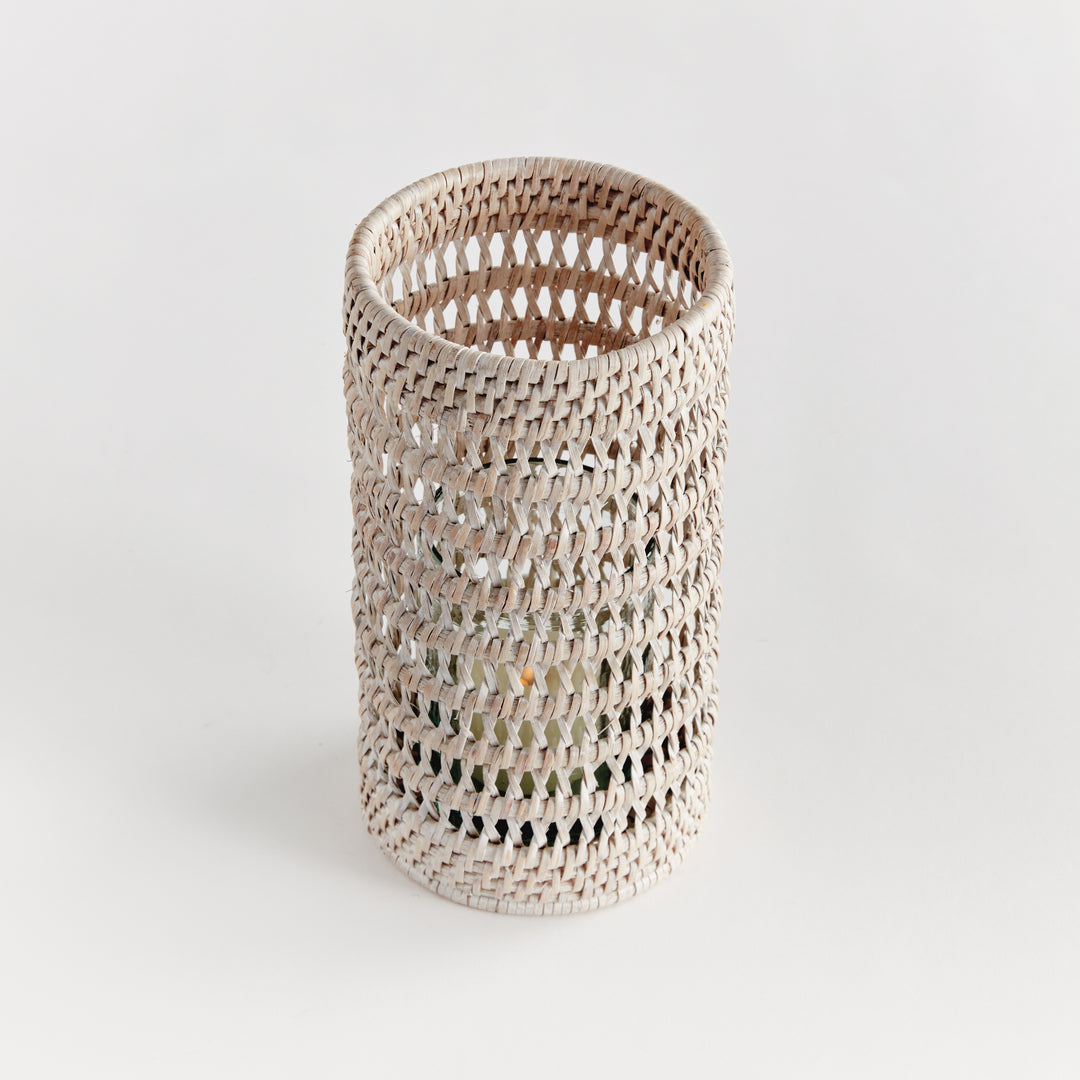 Angled view of a small whitewash rattan hurricane showing its open weave and cylindrical form on plain white, Transitional