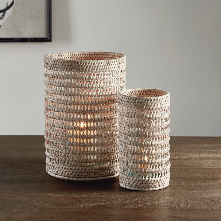 Small and large whitewash rattan hurricanes with candlelight inside, paired on a wooden console against a wall, Transitional