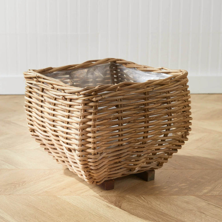 Square rattan planter basket with clear liner, placed on parquet floor with plant, woven indoor planter for casual home spaces – Casual Coastal.

