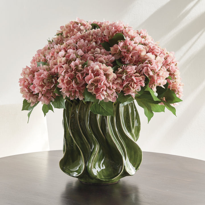 Sylva large green sculptural vase with pink hydrangea blooms on a dark round table in a pale interior setting. Modern Organic