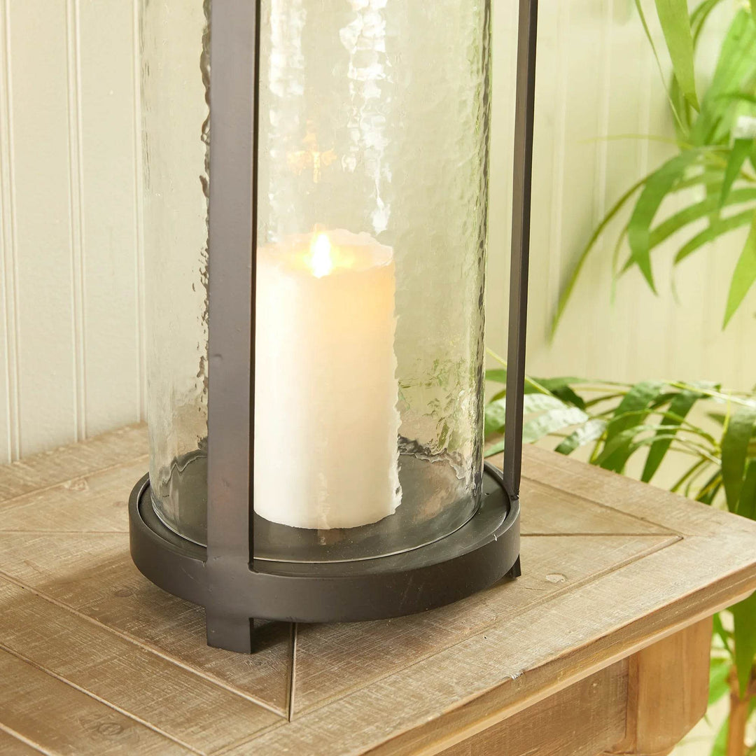Close up of tall black lantern with hammered glass and candle on wooden table, indoor decorative lantern for cozy ambiance.

