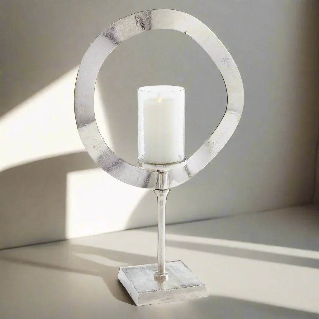 Tall silver candle stand with glass hurricane and LED candle styled in sunlight on tabletop, modern sculptural decor for home – Minimalist Glam.


