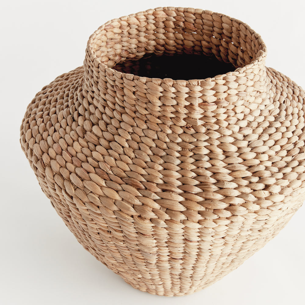 Angled view of Tamsin natural woven urn showing the open neck and broad water hyacinth shoulders in a light setting. Coastal