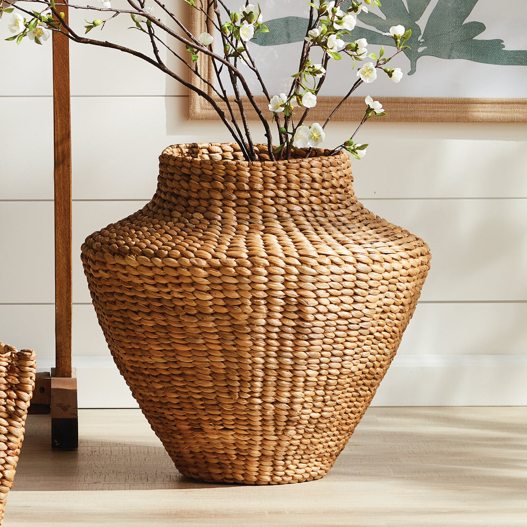 Tamsin natural woven urn holding white flowering branches near framed botanical artwork and white wall paneling. Coastal