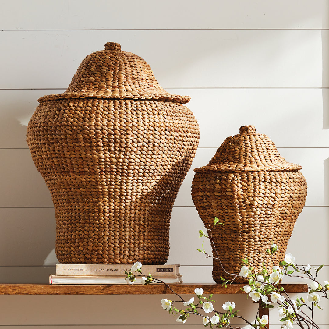 Tamsin natural woven ginger jar pair displayed on a wood shelf against white paneling with flowering branches nearby. Coastal