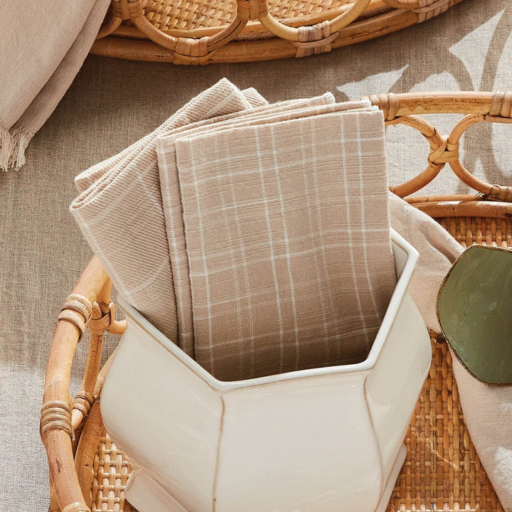 Taupe cotton dinner napkins with subtle arch grid pattern styled in a white crock with rattan trays table - Modern Organic.