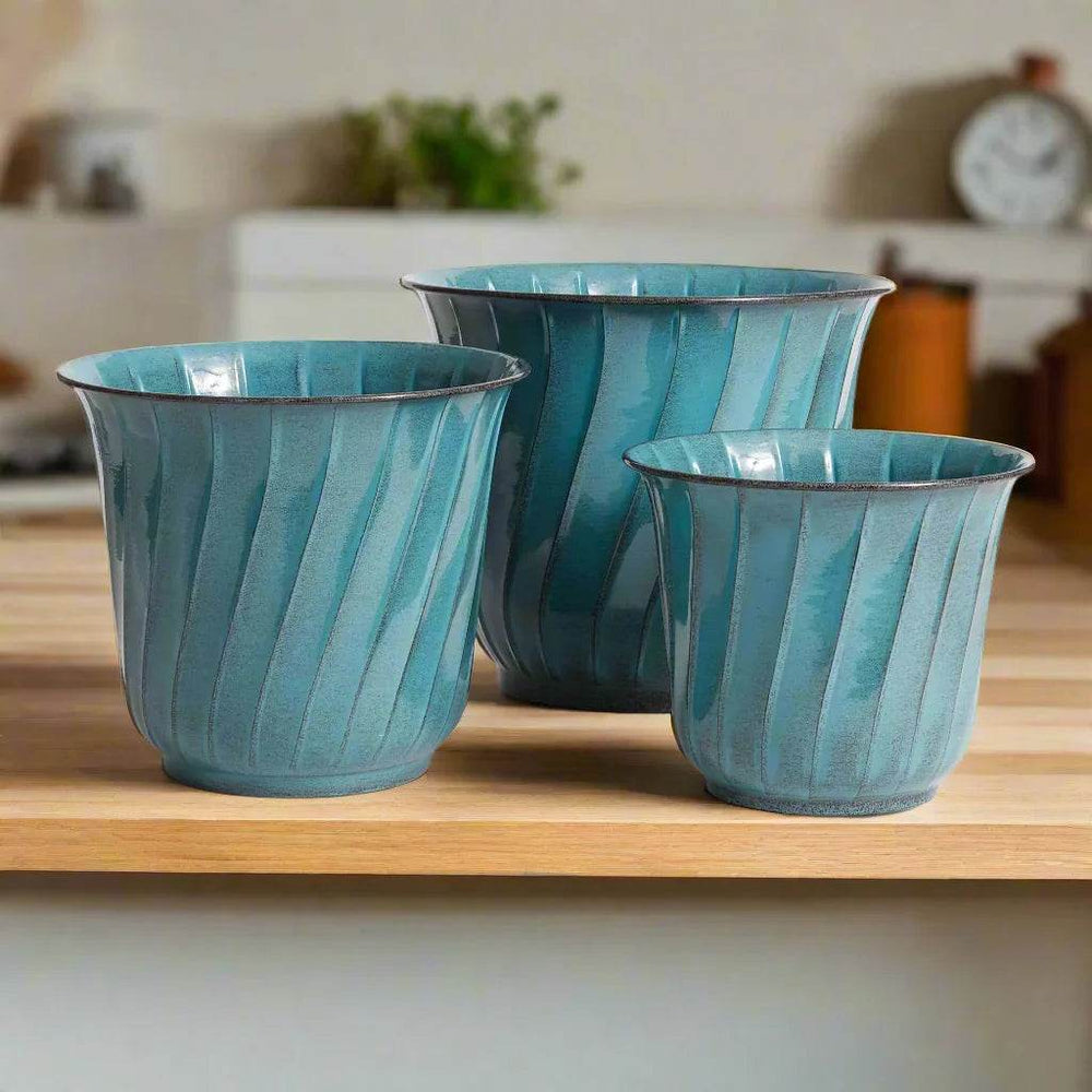 Teal metal planters with glossy enamel finish styled on a light wood surface with natural daylight in a modern organic setting.