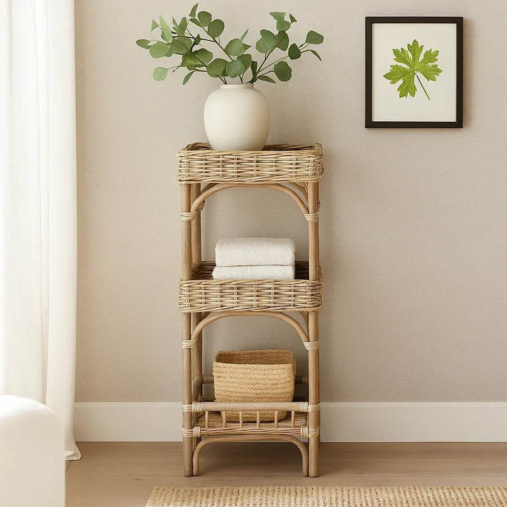 Three-tier wicker shelf styled in a coastal boho interior with soft natural lighting and textured panel walls.







