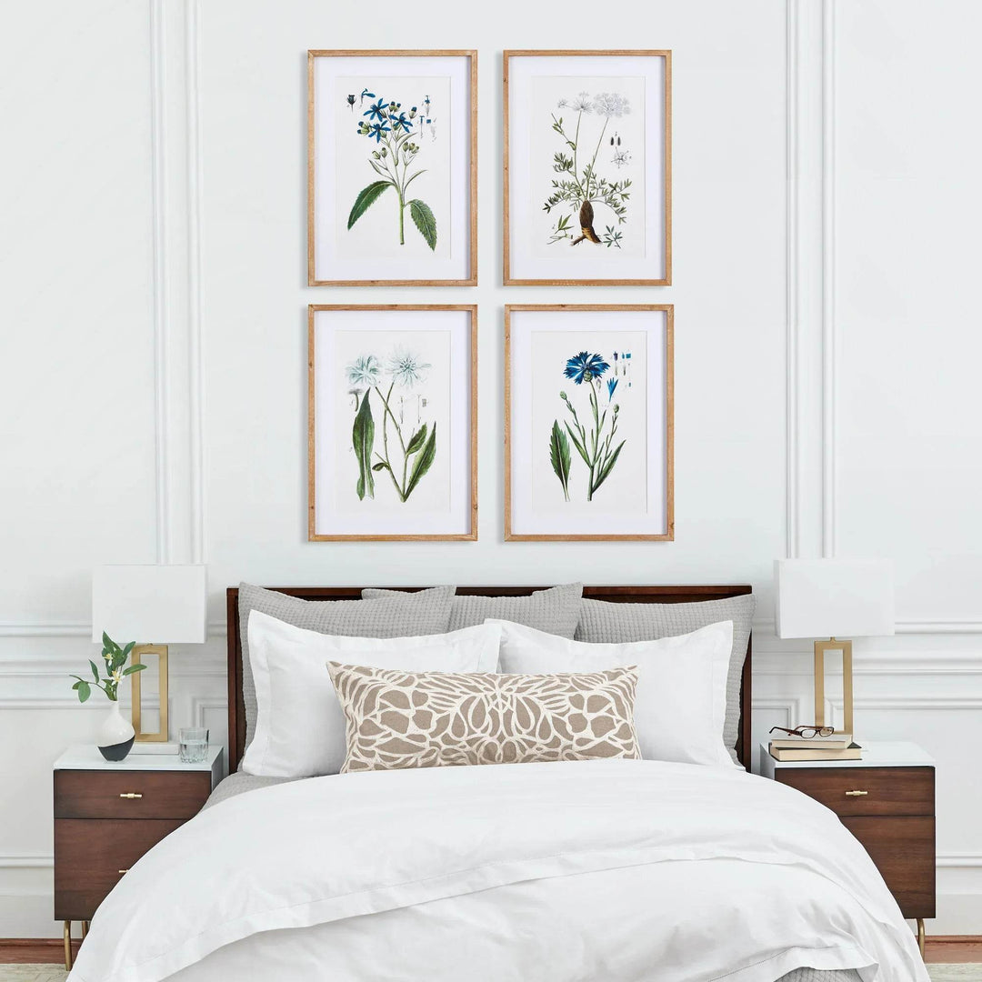 Traditional coastal botanical wall art styled above bed with white linens and wood nightstands.