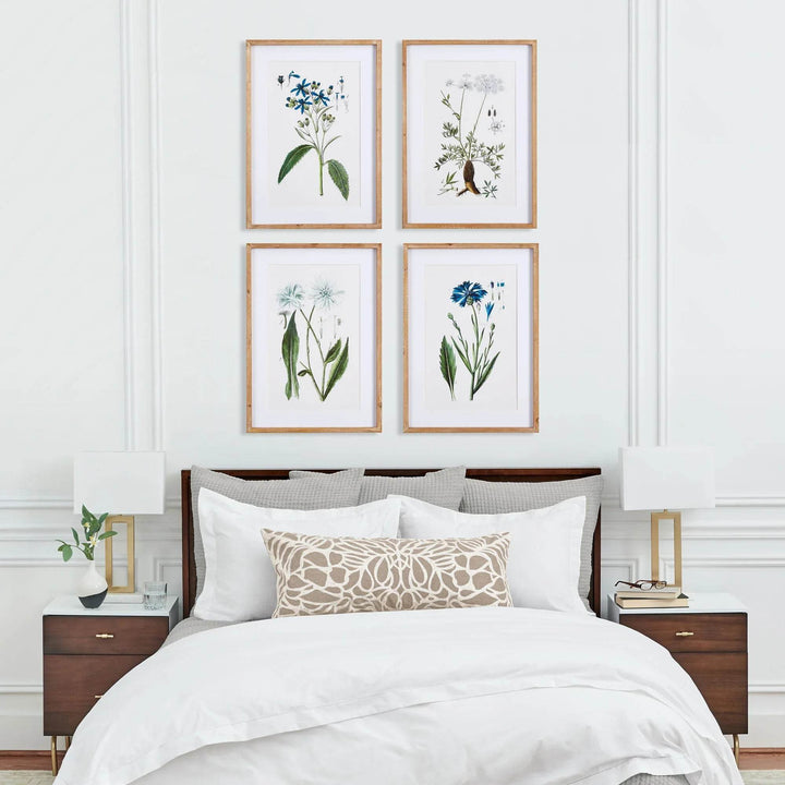 Traditional coastal botanical wall art styled above bed with white linens and wood nightstands.