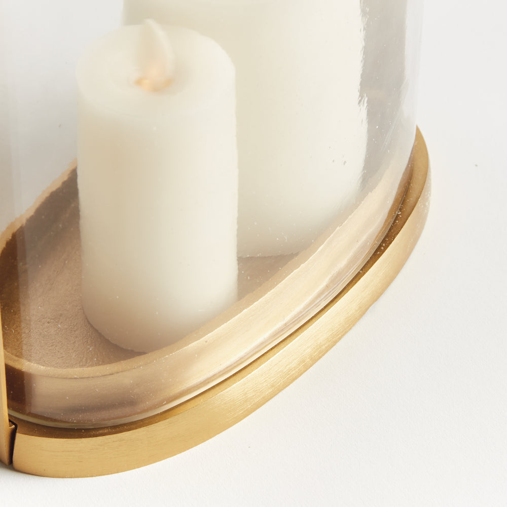 Close-up of the small transitional brass and glass hurricane candle holder showing matte brass oval base and candle detail.