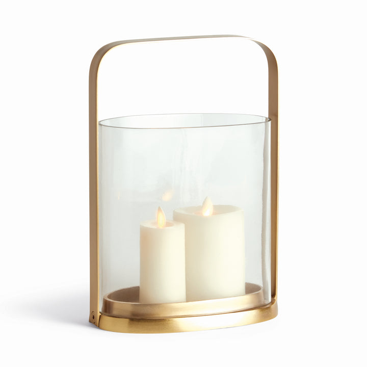Transitional small brass and glass hurricane candle holder with two white candles inside, front angled view.