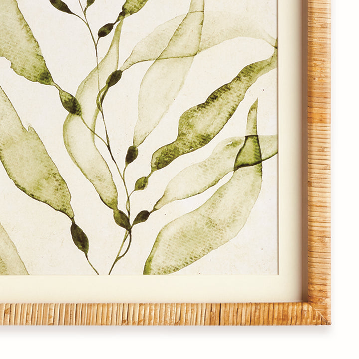 Detail of a green botanical print showing soft leaf shapes, ivory matting and the natural rattan-wrapped frame edge. Coastal