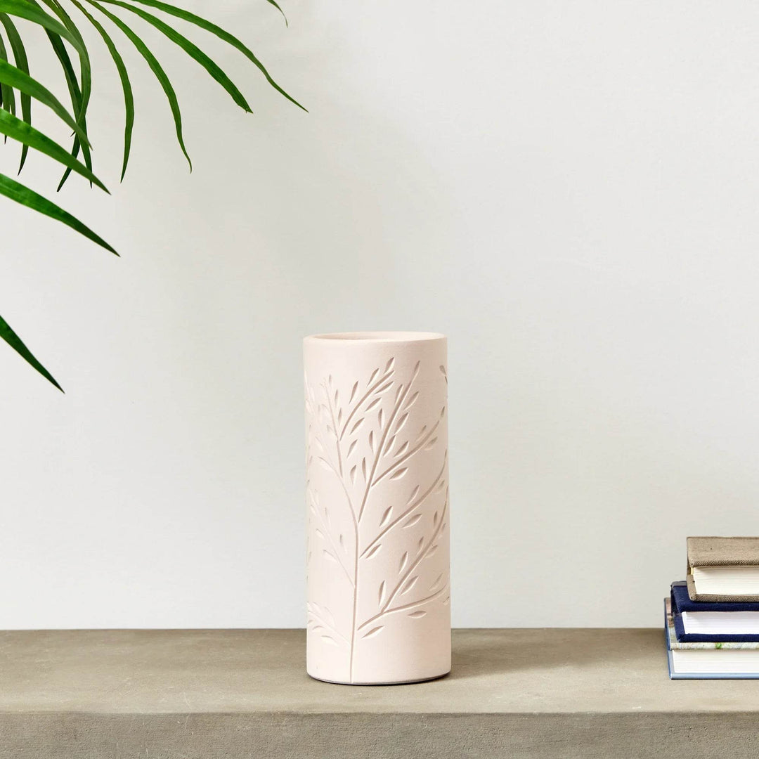 Handcrafted beige terracotta vine motif vase on tabletop with books, medium 9.5 inch cylinder vase for modern home styling.

