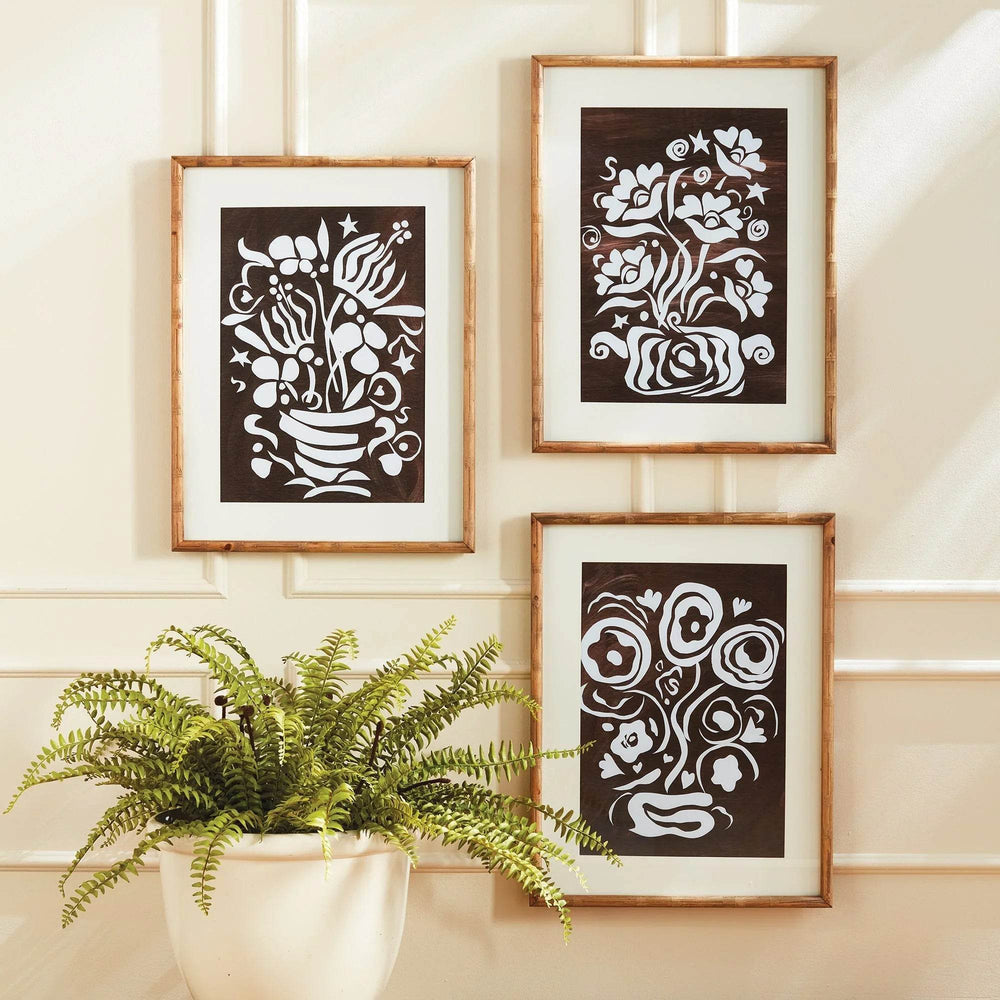 Vertical gallery display of framed vintage floral cutout prints in a warm-toned interior with potted fern accent
