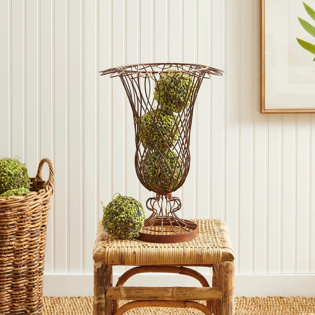Oversized wire vase with brown finish holding decorative greenery, styled on a rattan stool – Vintage Farmhouse style
