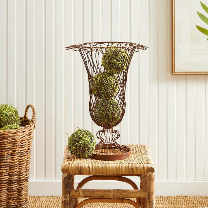 Oversized wire vase with brown finish holding decorative greenery, styled on a rattan stool – Vintage Farmhouse style