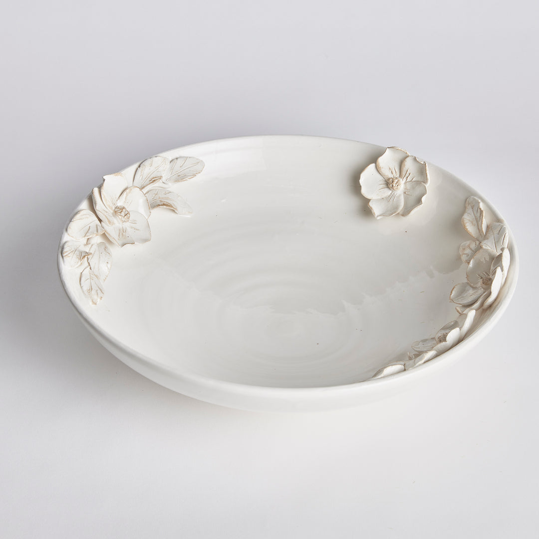 Angled view of a shallow white ceramic bowl with hand-applied dogwood flowers and leaves around the rim in Traditional style