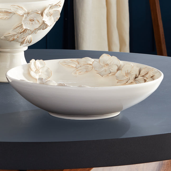 Shallow white floral ceramic bowl on a dark tabletop beside a matching pedestal bowl, styled together in Traditional style