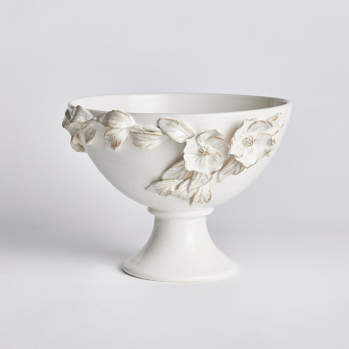 Angled view of a white ceramic pedestal bowl with a broad opening and hand-applied dogwood floral relief in Traditional style
