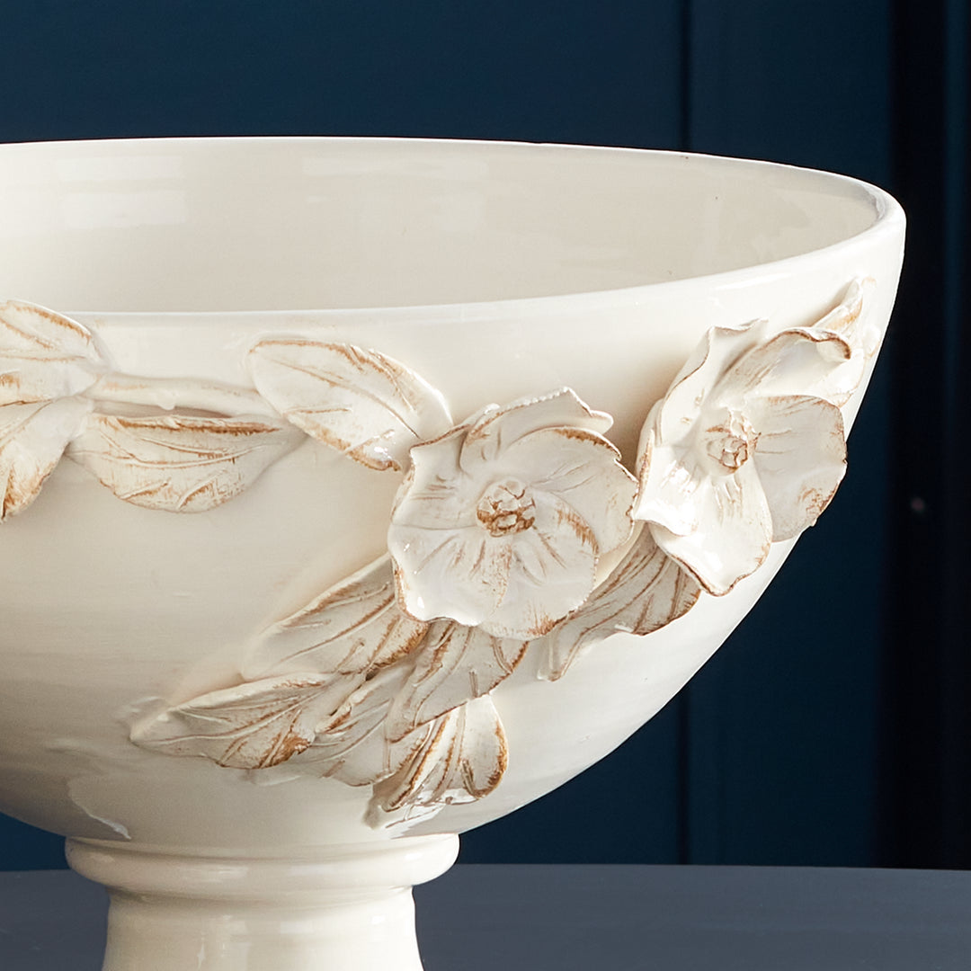 White floral ceramic pedestal bowl against a darker blue backdrop, showing raised flowers and leaves in Traditional style
