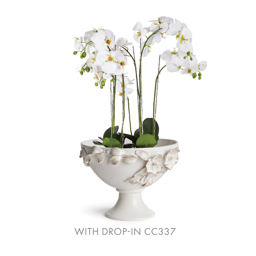 White ceramic footed bowl holding a white artificial orchid display, with leaves above the floral rim in Traditional style