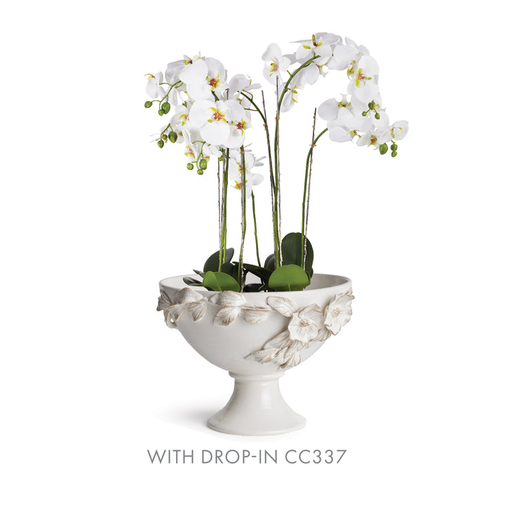 White ceramic footed bowl holding a white artificial orchid display, with leaves above the floral rim in Traditional style