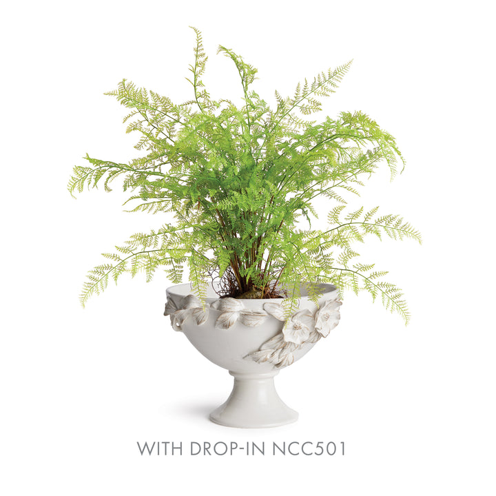 White ceramic floral footed bowl holding an artificial fern arrangement, with fronds spreading above it in Traditional style