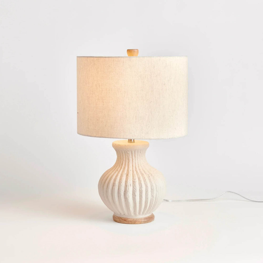Handcrafted cream wabi sabi lamp illuminated on white surface, showing soft glow and sculptural base detail