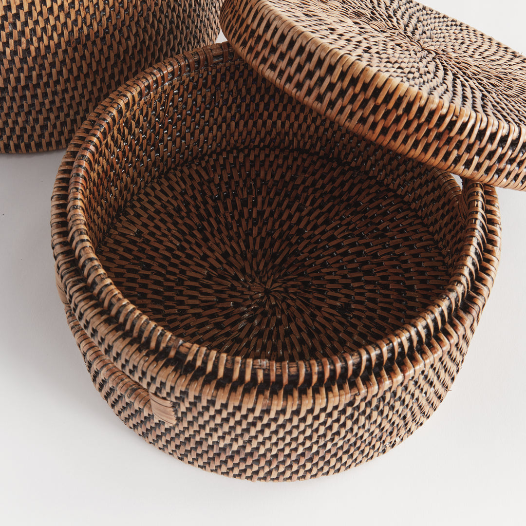 Overhead view of an open round warm brown rattan box showing the tightly woven interior and fitted lid beside it, Traditional