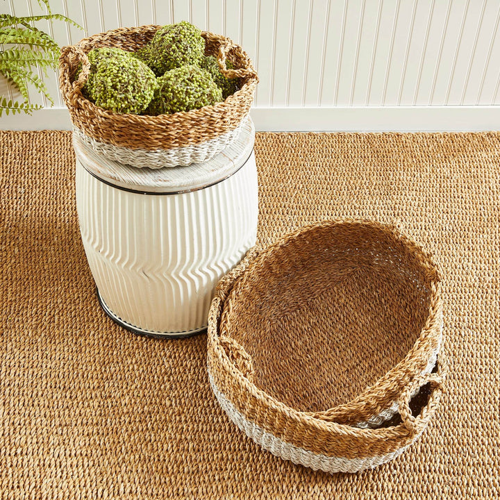 Low-profile seagrass baskets with white-dipped detail, displayed on a white garden stool with green accents – Coastal Casual.

