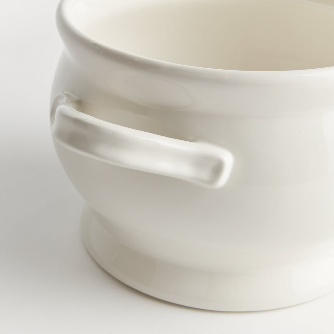 White ceramic footed bowl close-up showing a loop handle, rounded sides and a raised base beneath a curved rim - Traditional