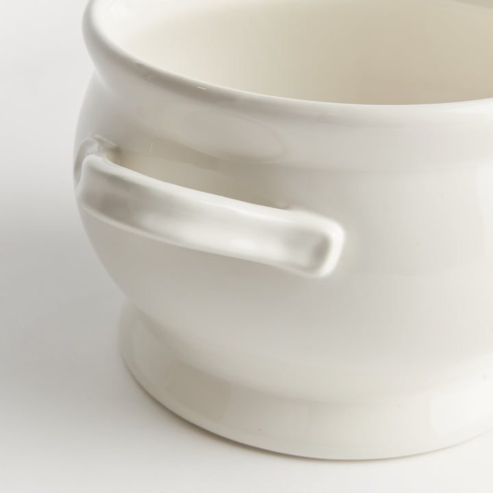 White ceramic footed bowl close-up showing a loop handle, rounded sides and a raised base beneath a curved rim - Traditional