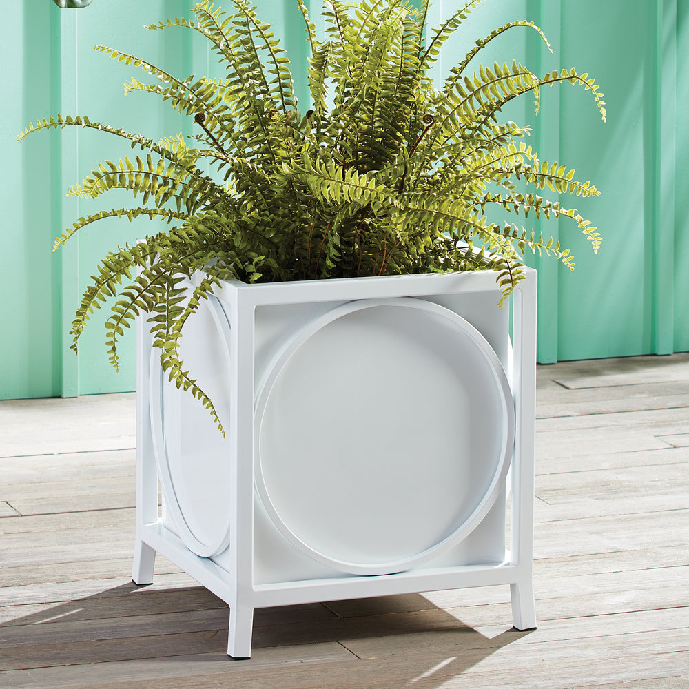 White coastal-style metal planter with fern, styled on sunlit patio against aqua siding.

