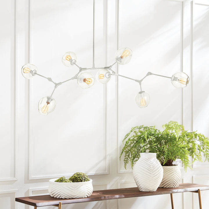 White mid-century modern chandelier styled above a wood console with greenery in a bright dining space.
