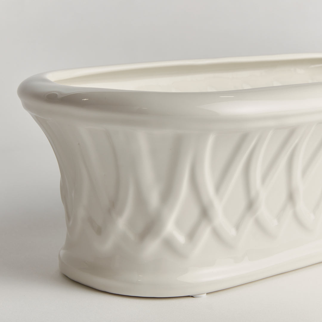 Close detail of a white oblong ceramic cachepot showing its raised basket-like pattern and curved upper rim, Traditional