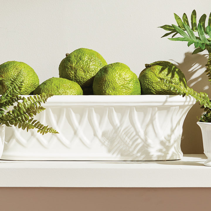 White oblong ceramic cachepot with raised basket-like relief holding green decorative orbs beside green foliage, Traditional