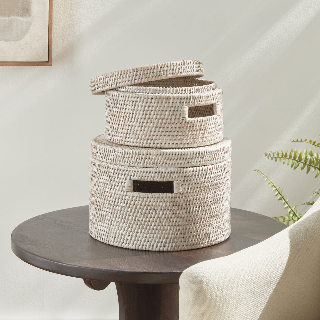 Two whitewash rattan lidded boxes stacked on a round table, with the upper lid lifted in a bright room, Coastal Transitional