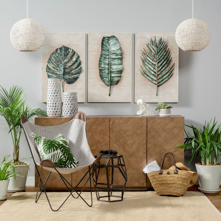 Whitewashed wood beaded pendant lights above a wood cabinet with leaf artwork, a lounge chair and green plants – Coastal