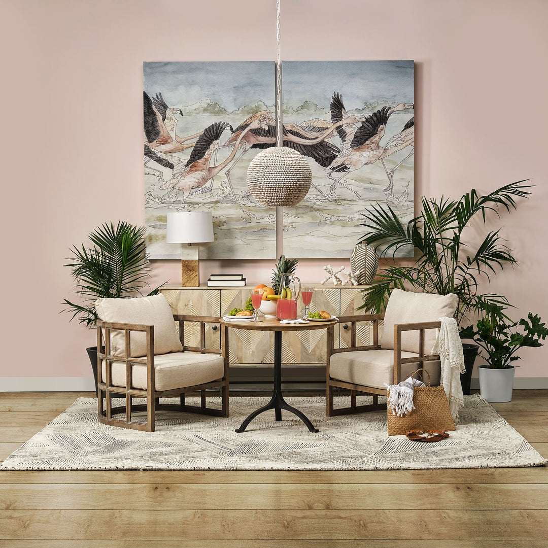 Wood beaded pendant light above a round dining table with upholstered chairs, plants and bird artwork on pink wall – Coastal