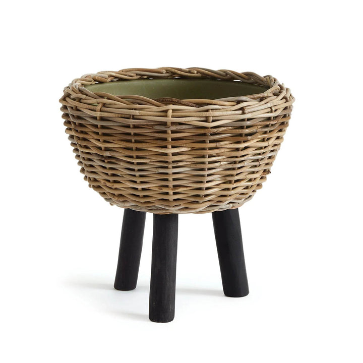 Rattan planter on three black teak legs, styled in clean minimal space
