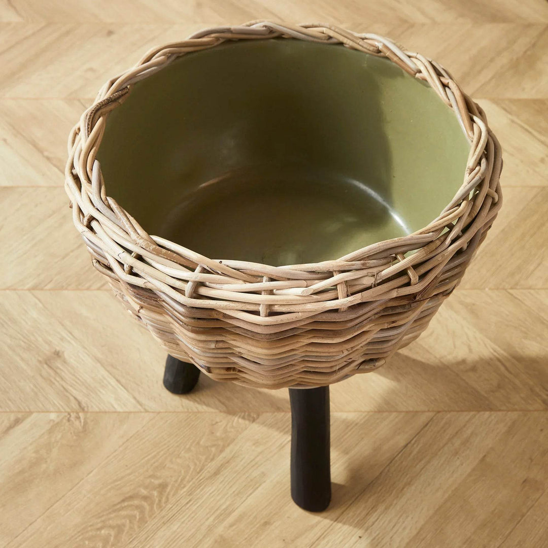 Interior view of green plastic liner inside woven rattan cachepot with legs

