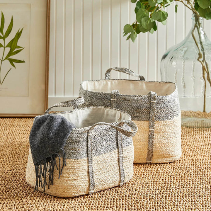 Pair of woven rectangular storage baskets placed indoors on a natural rug, neutral gray and beige weave with cotton liners.

