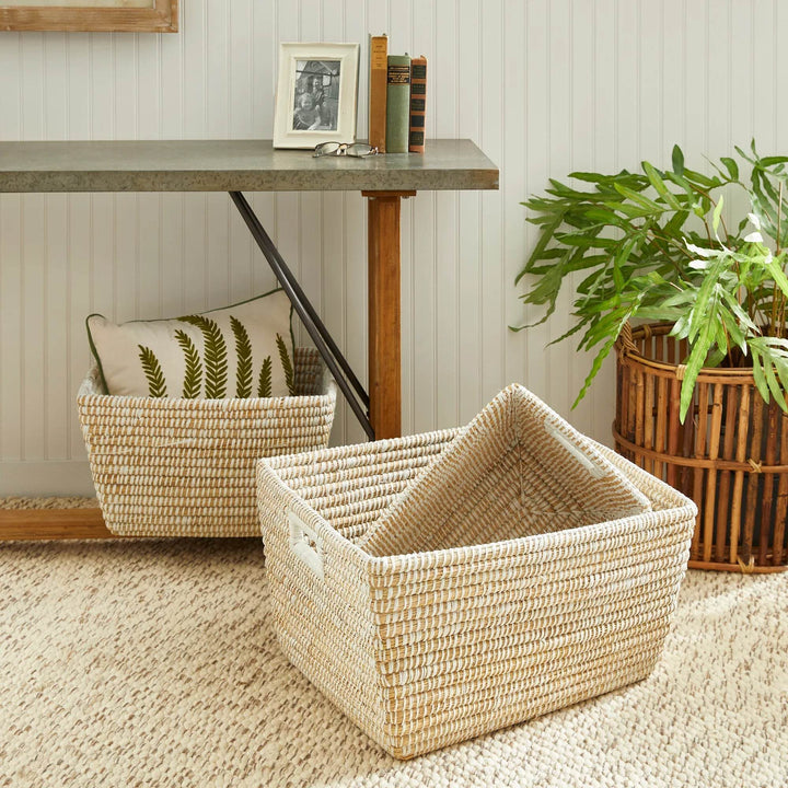 Woven baskets used under a desk for stylish storage, featuring natural fibers and white-wrapped handles in a coastal setting.