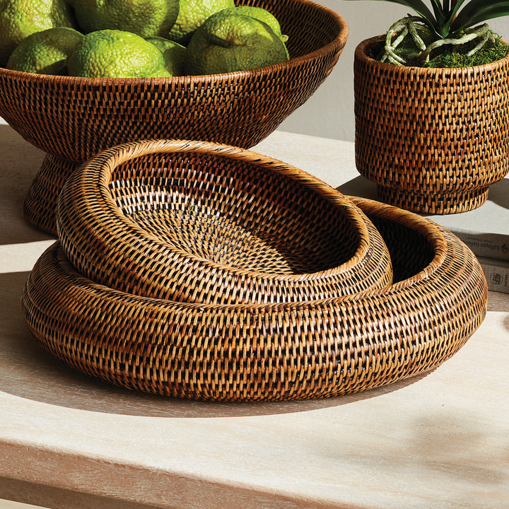 Brown rattan shallow display bowls stacked together beside other woven accessories on a pale table - Coastal Transitional